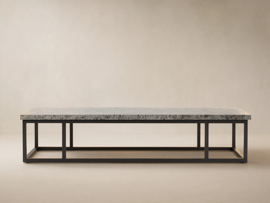 Paloma Outdoor Coffee Table with light gray speckled sintered stone top on a black rectangular metal frame, against a textured tan wall.