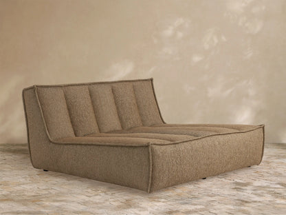 Light grey Porto Outdoor Collection Cover on a chaise lounge, draped with soft wrinkles, against a textured tan wall and brick patio.