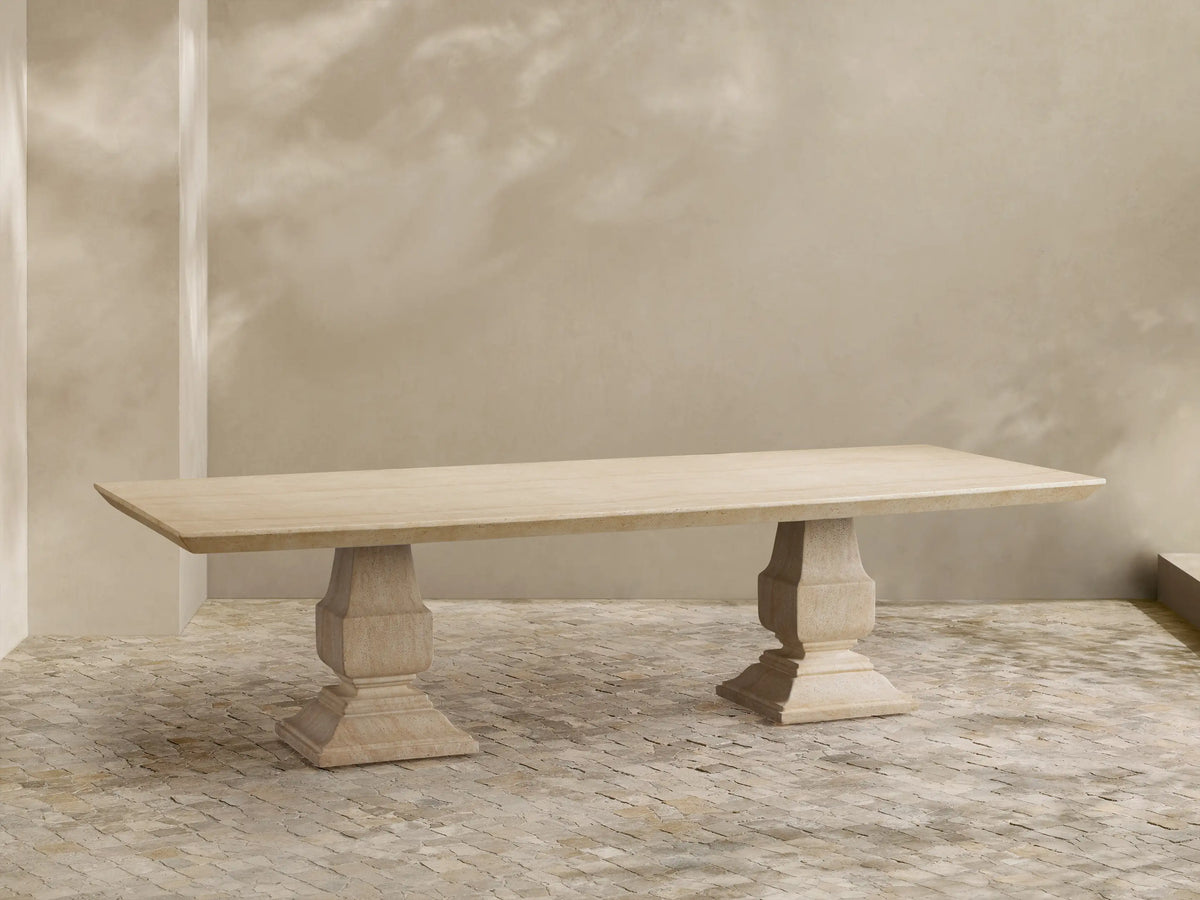Primrose Outdoor Dining Table, light beige stone rectangular table with two pedestal bases on a tiled patio, sun shadows.
