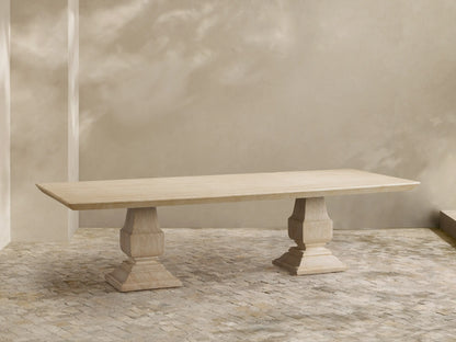 Primrose Outdoor Dining Table, light beige stone rectangular table with two pedestal bases on a tiled patio, sun shadows.