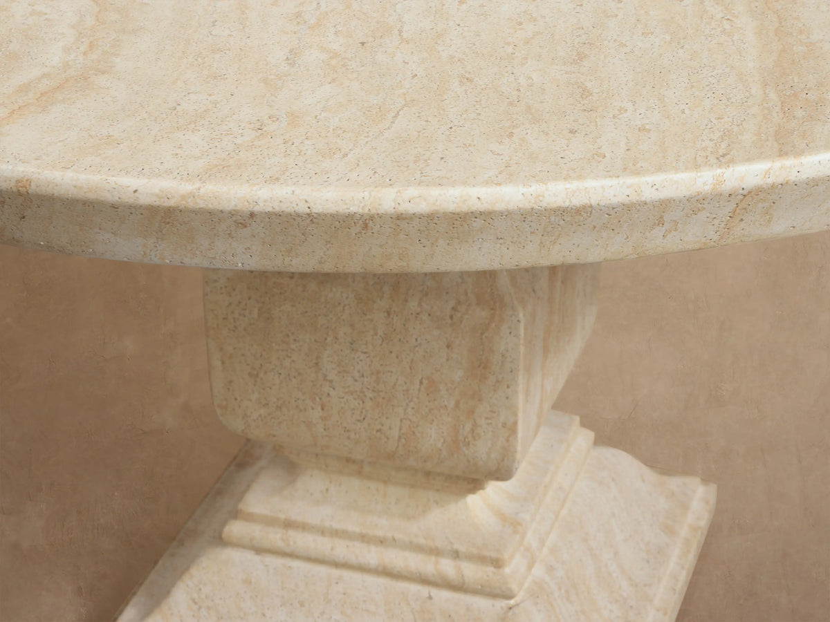 Round Primrose outdoor dining table, light beige concrete with stone texture and subtle veining, sturdy pedestal base on a patio.