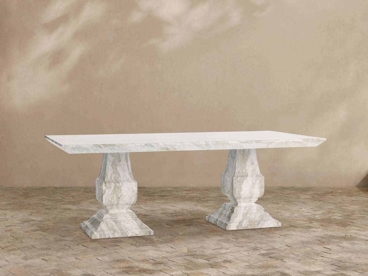 Primrose Outdoor Dining Table with rectangular white-grey marbled top and two sculpted pedestal bases on a tiled patio.
