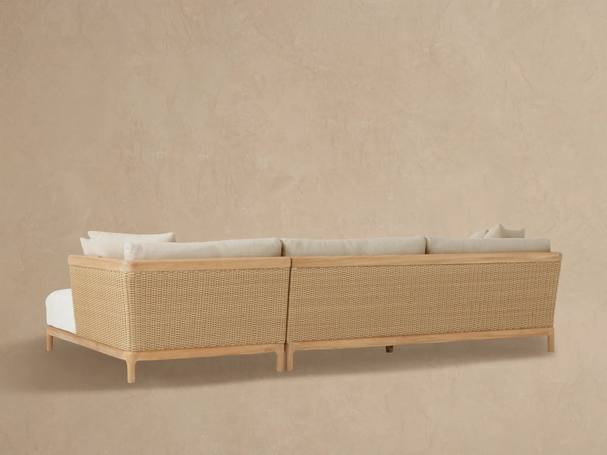 Close-up of Puglia Outdoor Teak Two-Piece Sectional chaise. Light beige textured cushions, natural teak arm, woven wicker panel.