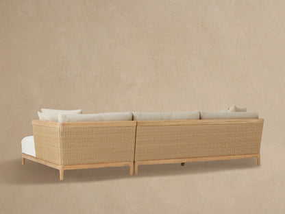 Close-up of Puglia Outdoor Teak Two-Piece Sectional chaise. Light beige textured cushions, natural teak arm, woven wicker panel.