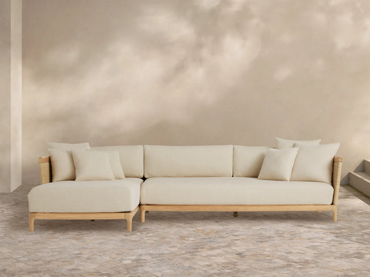 Puglia Outdoor Teak Two-Piece Sectional with Chaise, light teak L-shaped frame, cream cushions & toss pillows, woven accents.