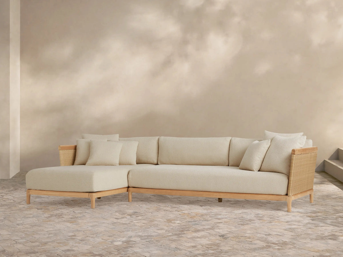 Puglia Outdoor Teak Two-Piece Sectional with Chaise, light teak L-shaped frame, cream cushions & toss pillows, woven accents.