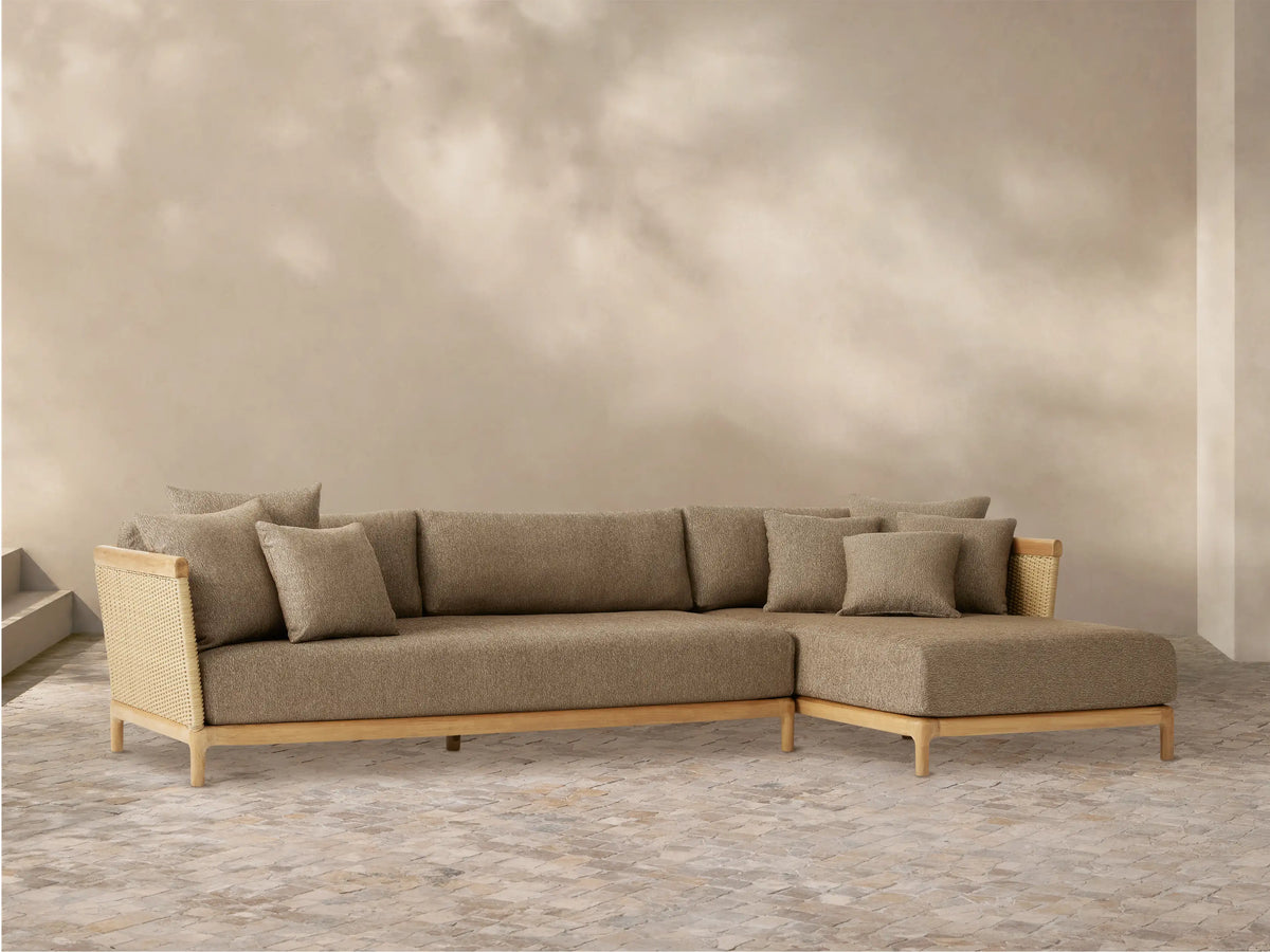 Puglia Outdoor Teak Sectional with chaise on right. Natural teak frame, woven wicker arms, light brown cushions and toss pillows.