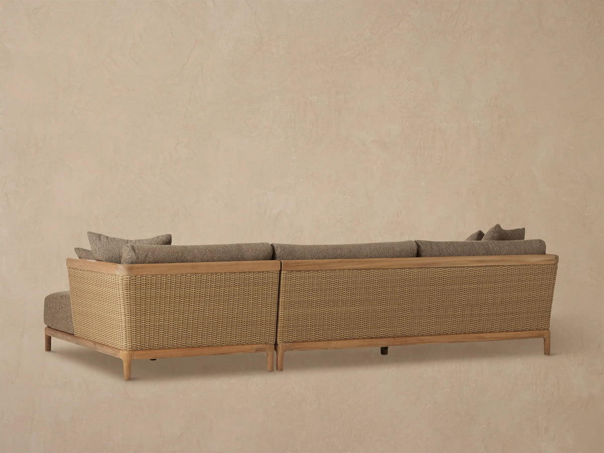 Close-up of Puglia Outdoor Teak Sectional armrest with light wood top, woven wicker side, and dark textured cushions.