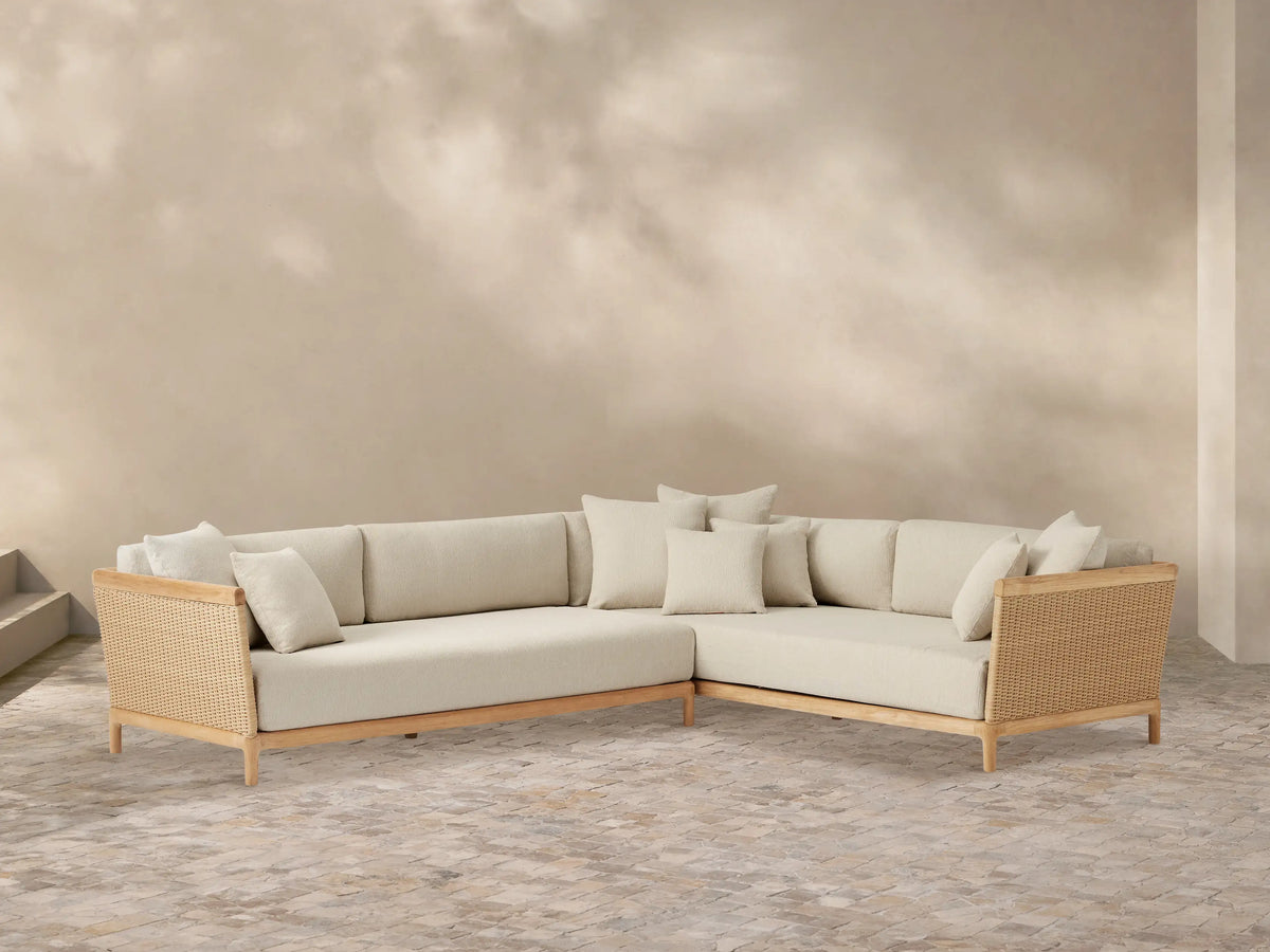 Puglia Outdoor Teak L-sectional sofa with natural teak wood frame, woven wicker, and light cream cushions on a textured patio.