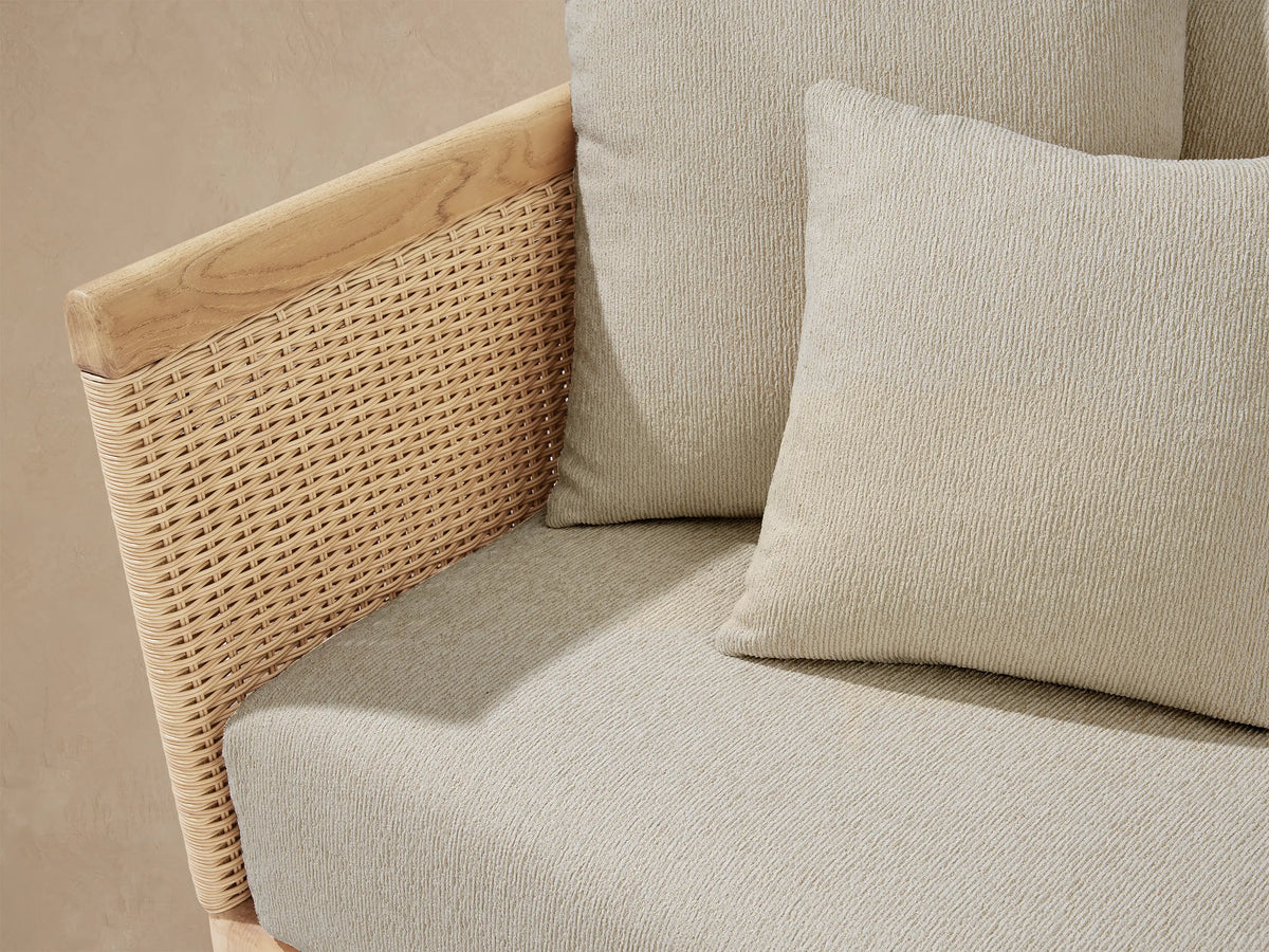 L-shaped Puglia Outdoor Teak Two-Piece Sectional with light beige cushions, teak frame, and woven rattan sides on a stone patio.