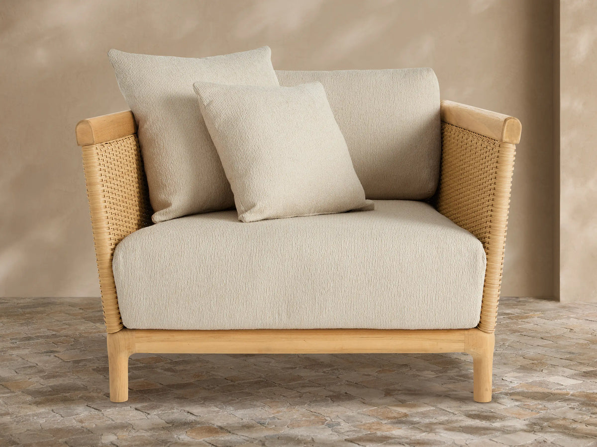 Light grey Puglia Outdoor Collection Cover tailored over a chair. Textured fabric with central seam, on a stone patio against a warm wall.