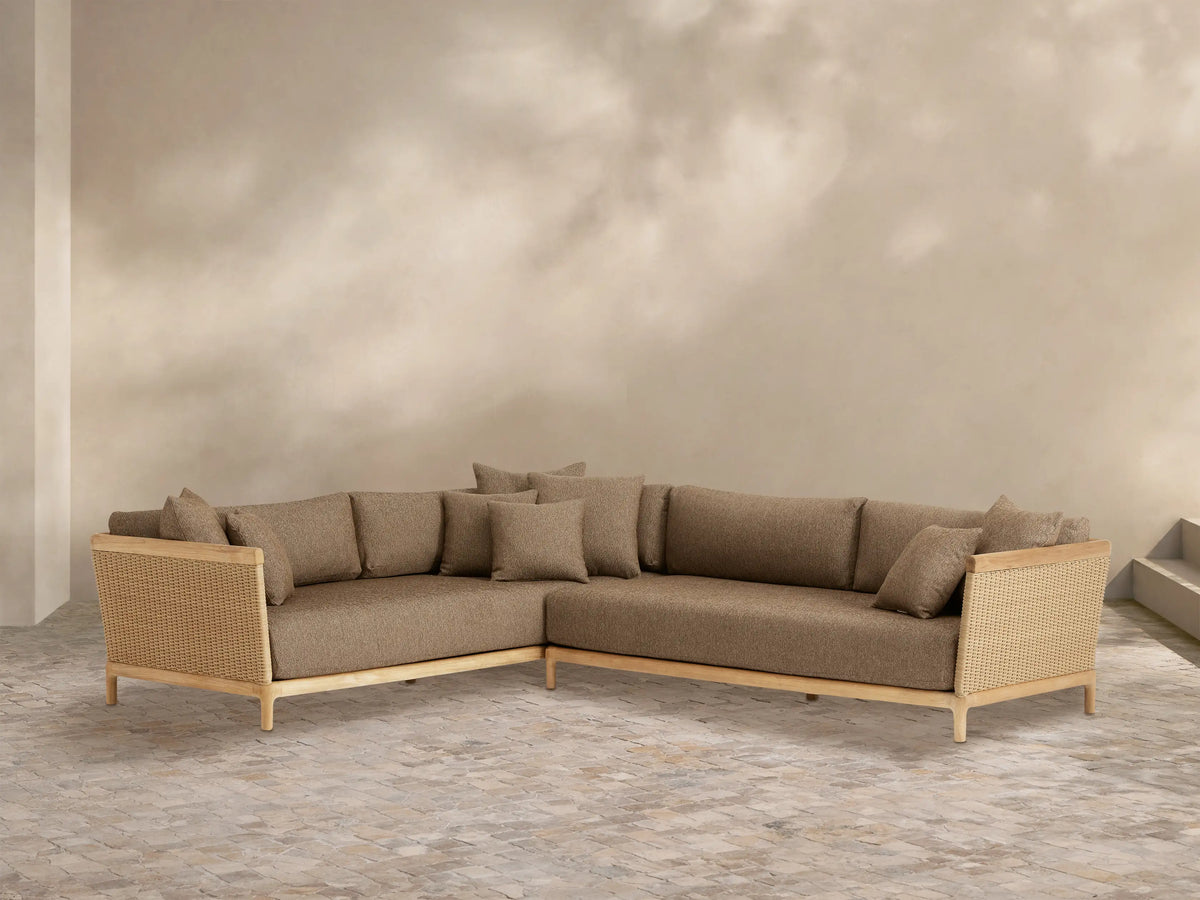 Puglia Outdoor Teak L-shaped sectional with natural teak frame, woven wicker sides, light brown cushions, and throw pillows on a patio.