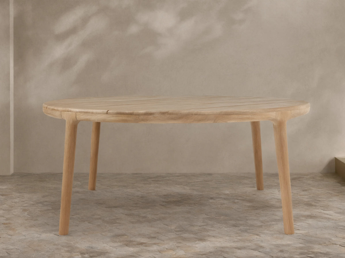 Puglia Outdoor Teak Round Dining Table, light natural wood, slatted round top, four sturdy legs on a tiled patio.