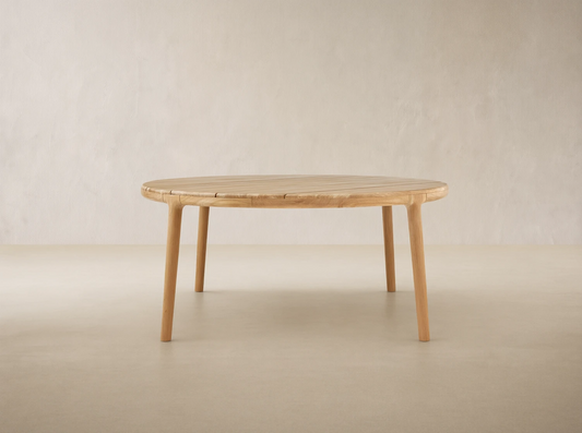 Puglia Outdoor Teak Round Dining Table, light natural wood, slatted round top, four sturdy legs on a tiled patio.