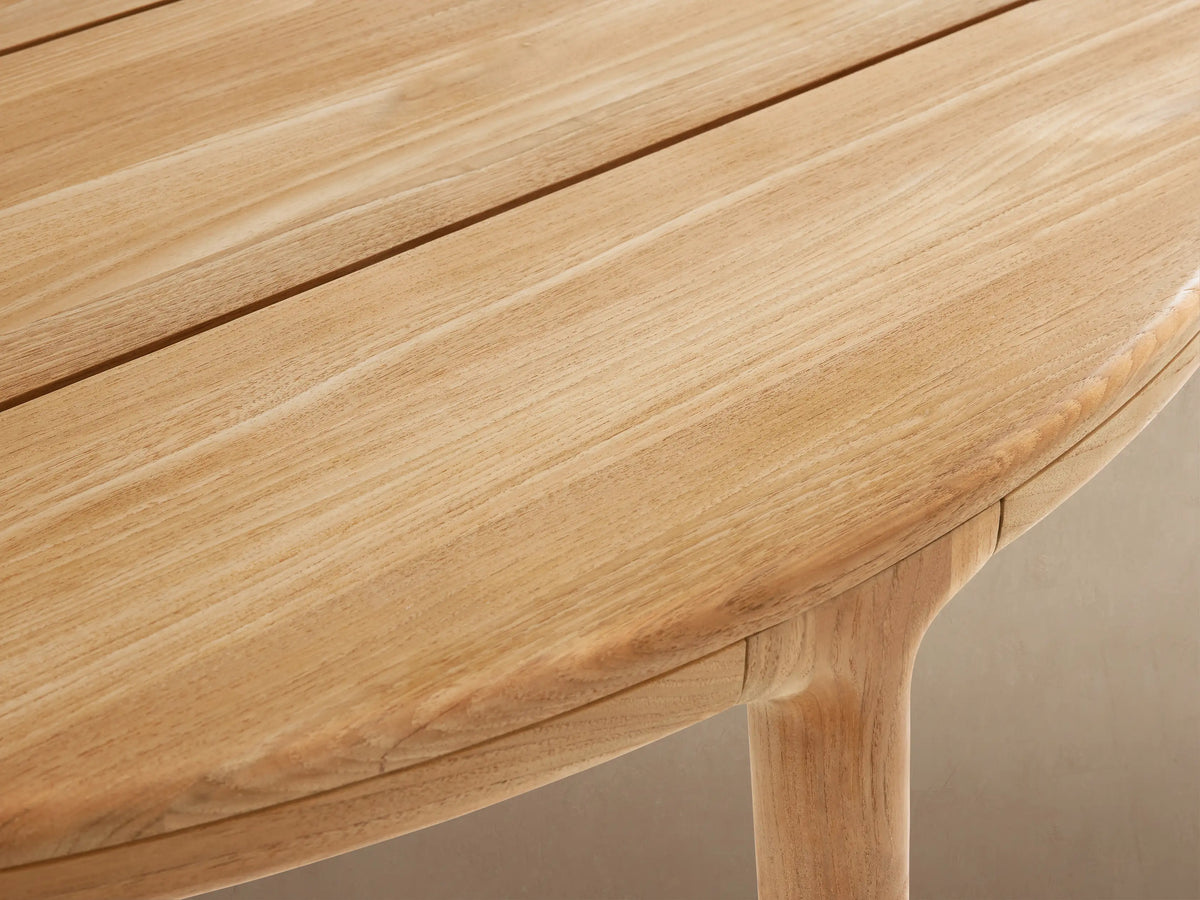 Puglia Outdoor Teak Round Dining Table, light natural wood, slatted round top, four sturdy legs on a tiled patio.