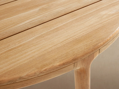 Puglia Outdoor Teak Round Dining Table, light natural wood, slatted round top, four sturdy legs on a tiled patio.