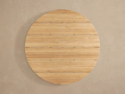 Detail of Puglia Outdoor Teak Round Dining Table. Golden, unfinished teak wood with visible grain, curved edge, and leg.