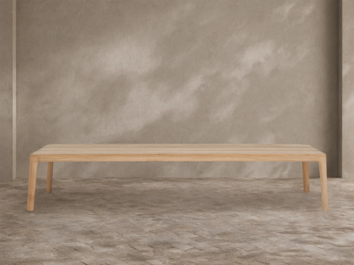 Puglia Outdoor Teak Coffee Table, light golden untreated teak wood, rectangular slatted top, sturdy legs, on stone patio.