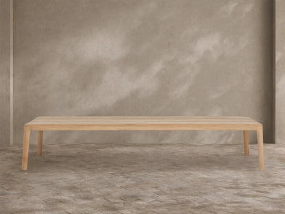 Puglia Outdoor Teak Coffee Table, light golden untreated teak wood, rectangular slatted top, sturdy legs, on stone patio.