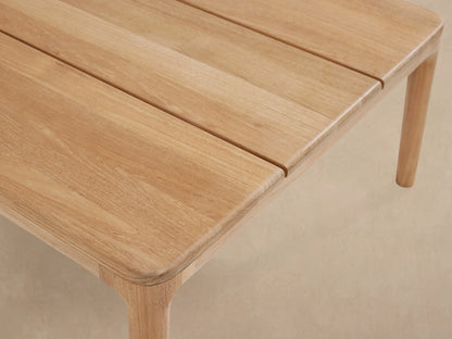 Puglia Outdoor Teak Coffee Table: A long, rectangular, slatted table of light natural teak wood on a stone patio.
