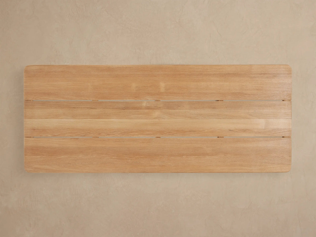 Close-up angled view of Puglia Outdoor Teak Coffee Table, showing light blonde slatted top with natural wood grain and rounded edges.