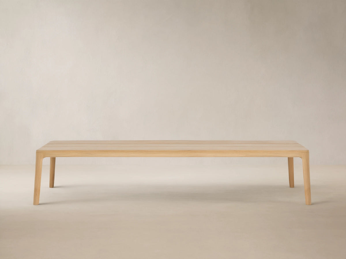 Puglia Outdoor Teak Coffee Table, light golden untreated teak wood, rectangular slatted top, sturdy legs, on stone patio.
