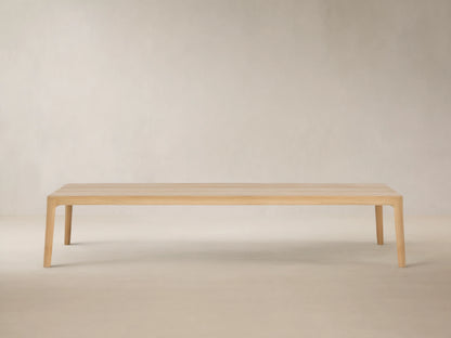 Puglia Outdoor Teak Coffee Table, light golden untreated teak wood, rectangular slatted top, sturdy legs, on stone patio.