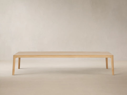 Puglia Outdoor Teak Coffee Table, light golden untreated teak wood, rectangular slatted top, sturdy legs, on stone patio.