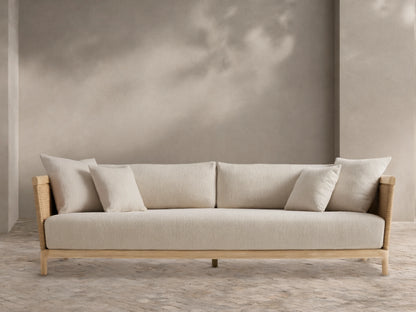 Puglia Outdoor Teak Sofa, light-toned wood frame, woven sides, cream cushions & pillows, on a patterned patio floor before a beige wall.