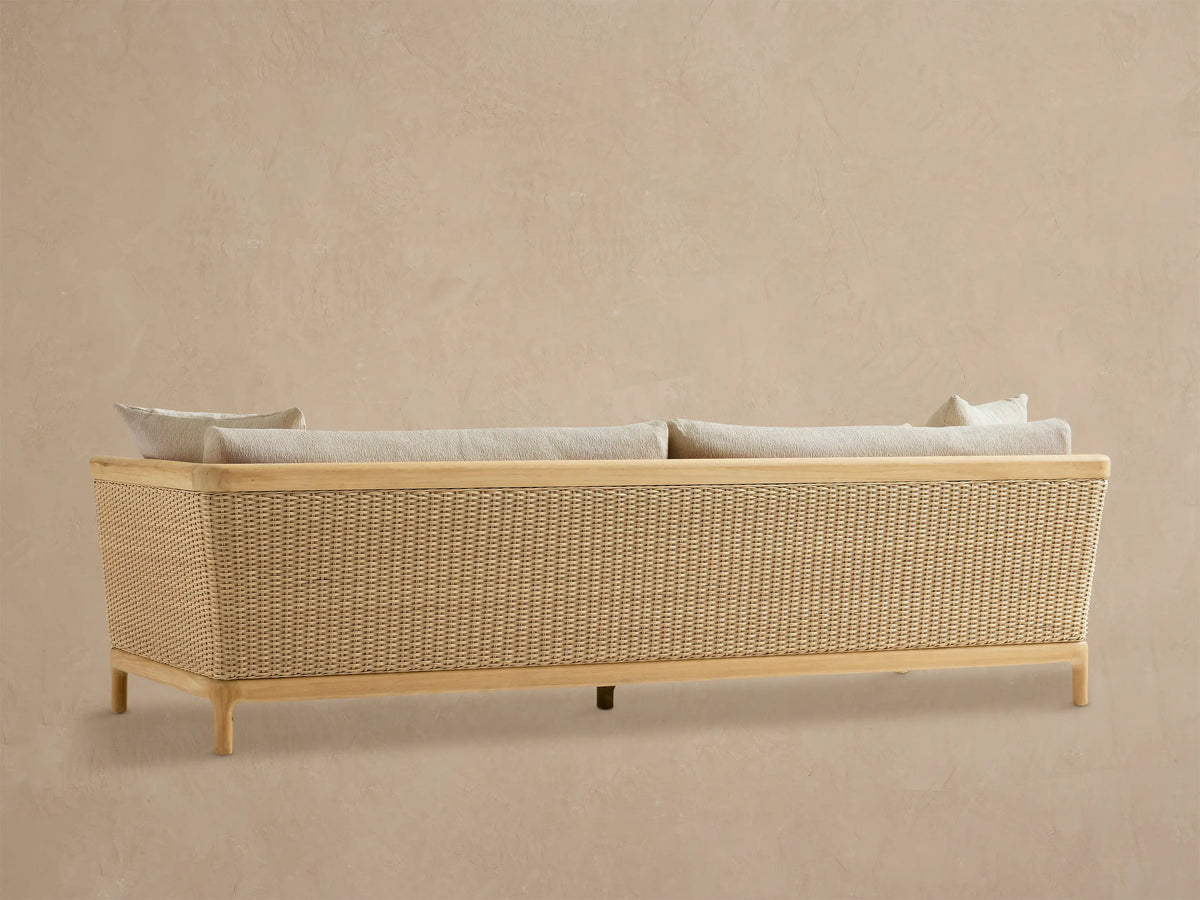 Close-up of Puglia Outdoor Teak Sofa, featuring a smooth teak arm, woven light-colored wicker, and plush cream cushions.