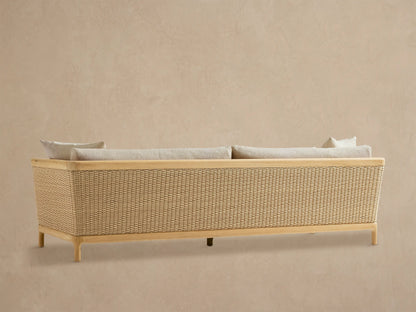 Close-up of Puglia Outdoor Teak Sofa, featuring a smooth teak arm, woven light-colored wicker, and plush cream cushions.
