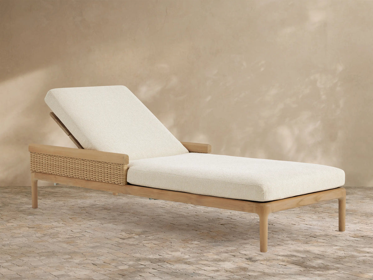 Puglia Outdoor Teak Chaise with reclined backrest, light cream cushions, & woven side panel on patio.