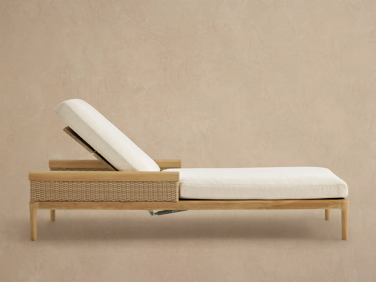 Puglia Outdoor Teak Chaise with reclined backrest, light cream cushions, & woven side panel on patio.