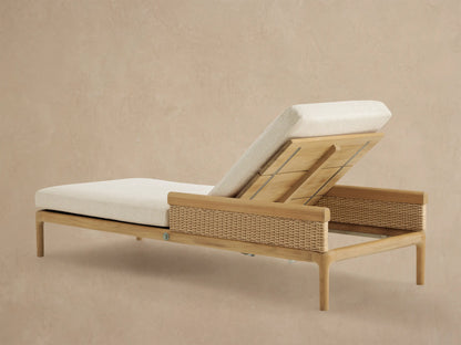 Close-up of Puglia Outdoor Teak Chaise. Golden teak armrest, woven tan wicker, and cream cushions in a reclined position.