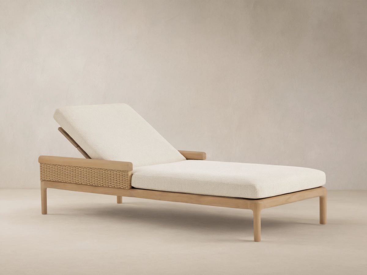 Puglia Outdoor Teak Chaise with reclined backrest, light cream cushions, & woven side panel on patio.