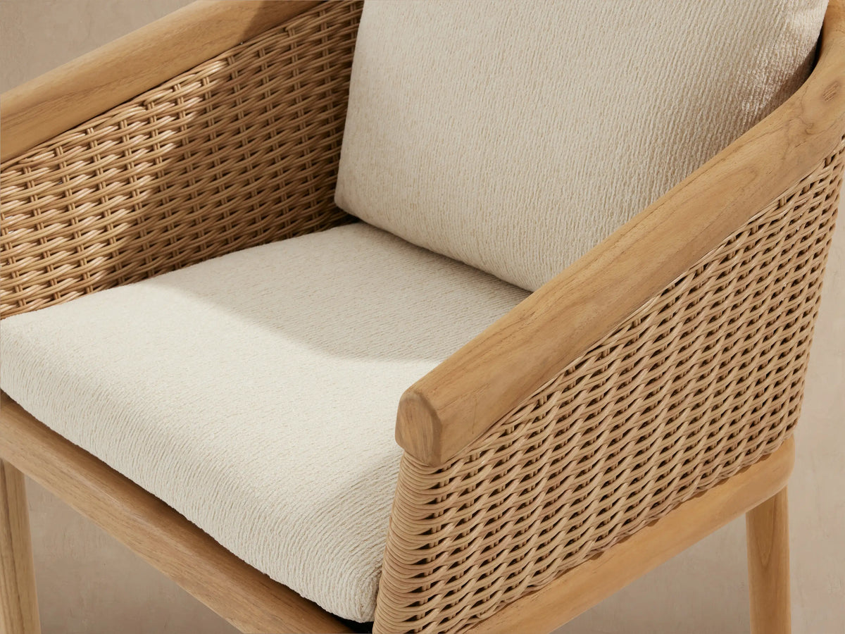 Front view of Puglia Outdoor Teak Dining Chair. Natural teak frame, light woven wicker back, and two cream outdoor cushions.