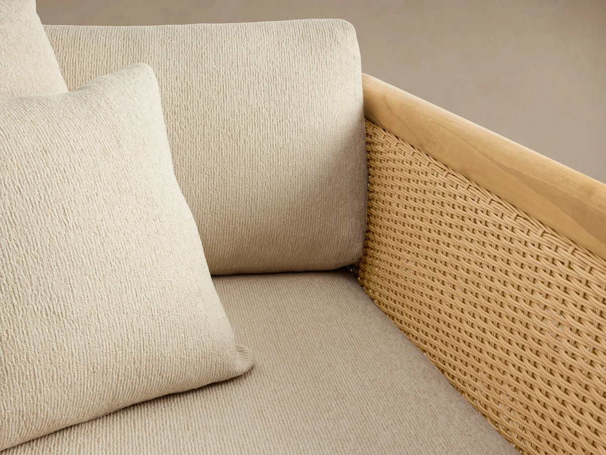 Puglia Outdoor Teak Lounge Chair with natural teak frame, tan woven wicker sides, and light beige cushions with two pillows.
