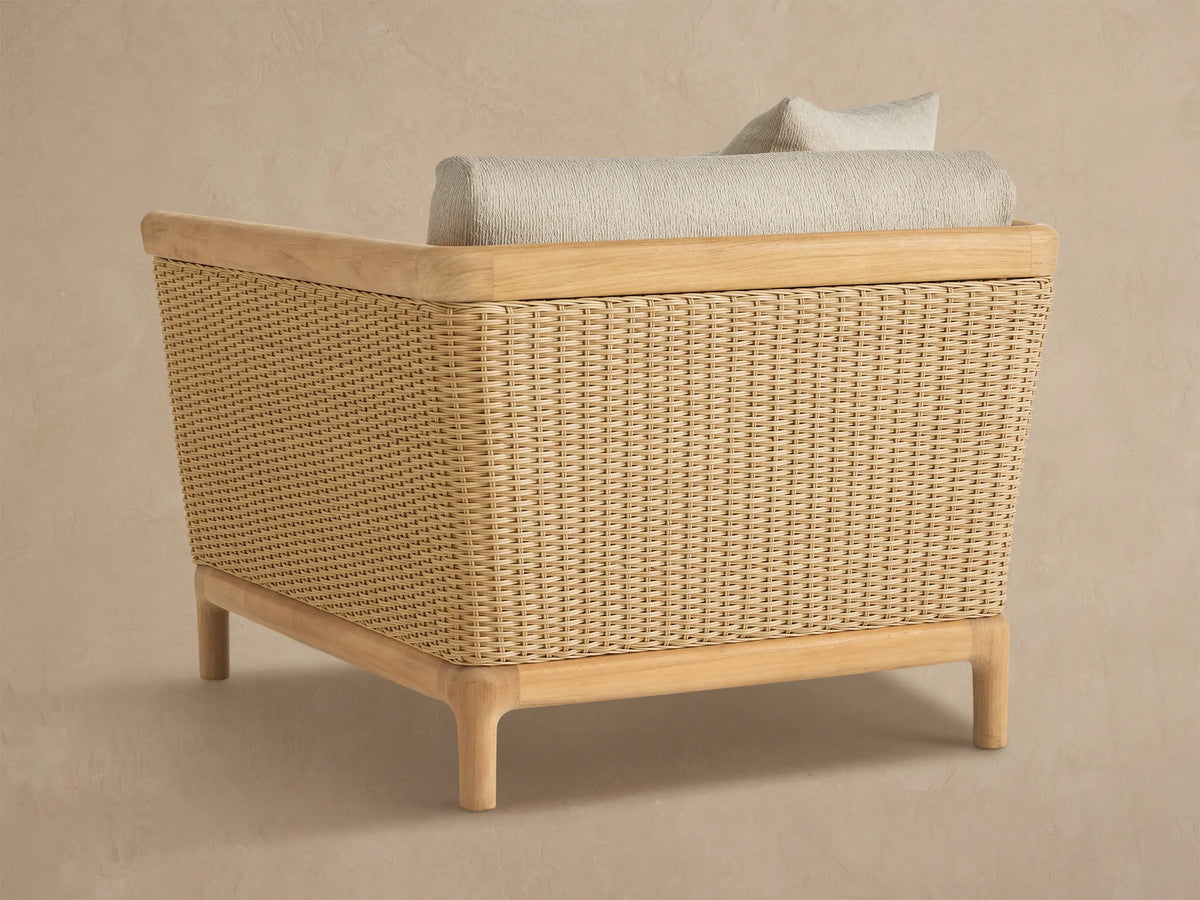 Puglia Outdoor Teak Lounge Chair close-up. Beige cushions, natural teak armrest, woven tan resin wicker side panel.