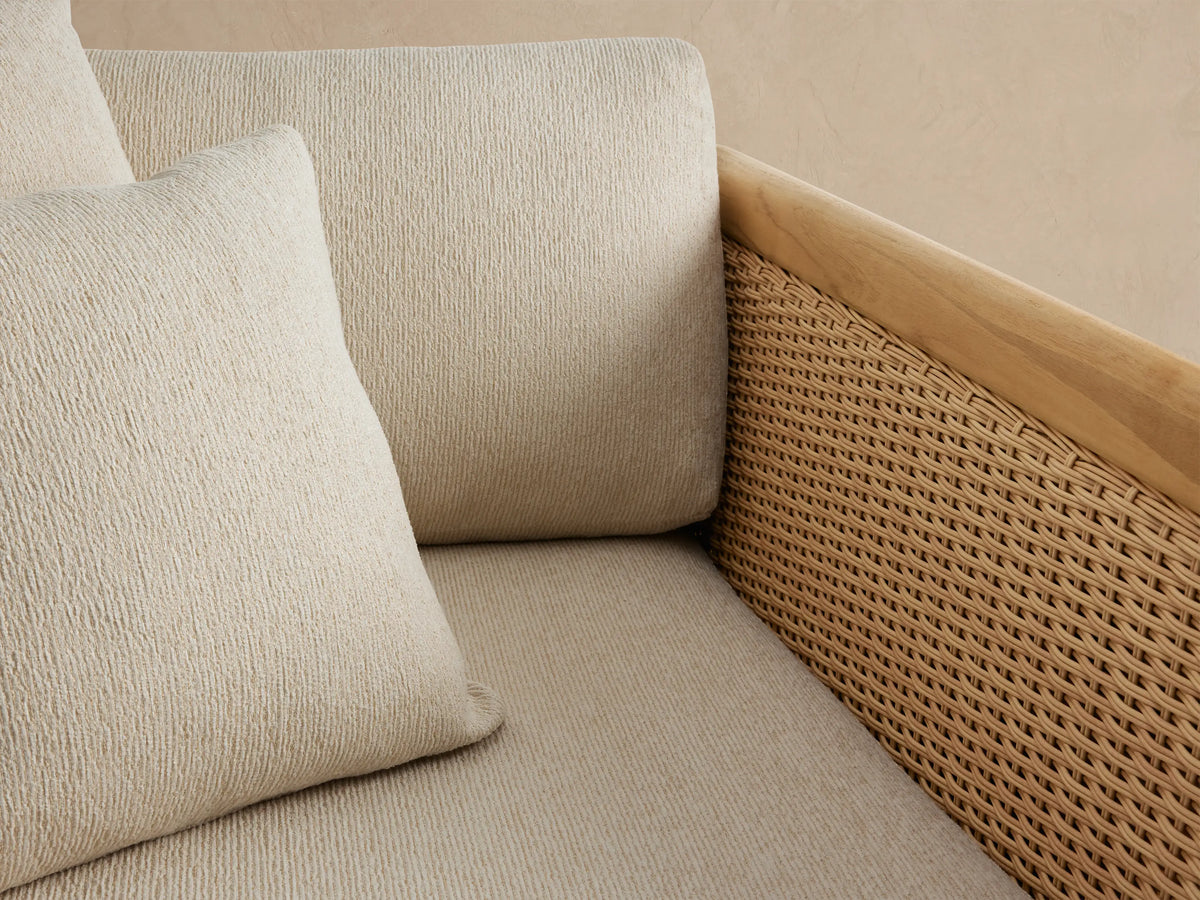 Puglia Outdoor Teak Lounge Chair with natural teak frame, woven wicker sides, and light cream cushions on a stone patio.