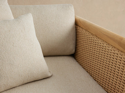Puglia Outdoor Teak Lounge Chair with natural teak frame, woven wicker sides, and light cream cushions on a stone patio.