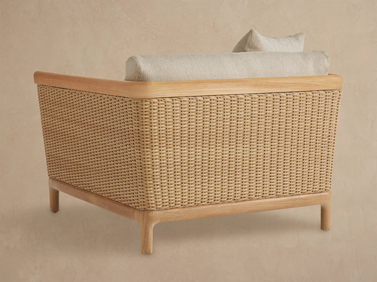 Puglia Outdoor Teak Lounge Chair. Close-up shows light beige textured cushions, natural teak armrest, and woven wicker side.