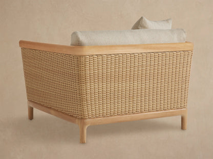 Puglia Outdoor Teak Lounge Chair. Close-up shows light beige textured cushions, natural teak armrest, and woven wicker side.