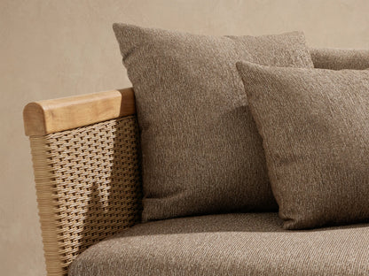 Angled Puglia Outdoor Teak Sofa with natural wood frame, woven sides, and soft textured beige-brown cushions and toss pillows.