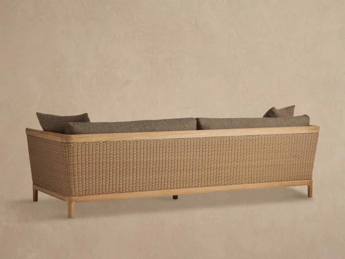Puglia Outdoor Teak Sofa arm with light teak wood top, woven tan wicker, and textured brown fabric cushions.