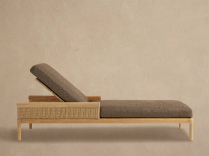 Puglia Outdoor Teak Chaise with natural wood frame, woven side panel, and dark taupe cushions, reclined on a patio.