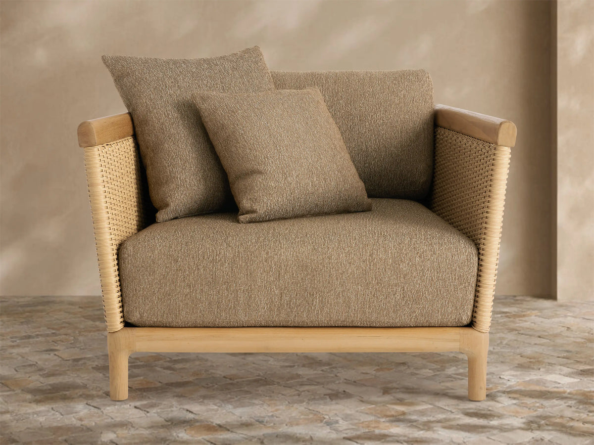 Puglia Outdoor Teak Lounge Chair, light natural teak wood frame, tan woven sides, and plush light brown cushions, on a tiled patio.