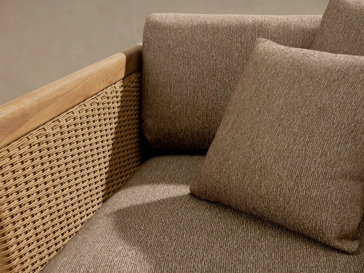 Puglia Outdoor Teak Lounge Chair with natural teak frame, handwoven light brown wicker sides, and heathered brown cushions with two toss pillows.