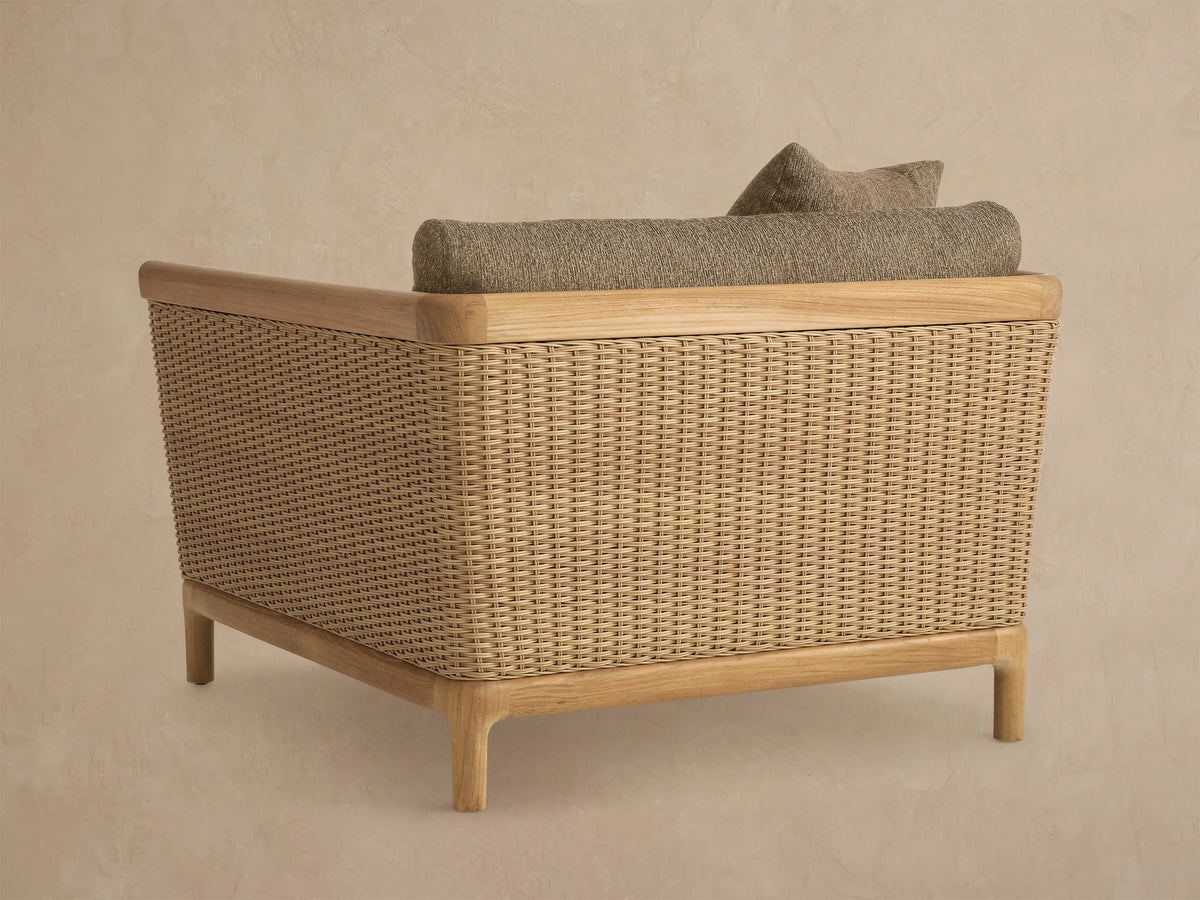 Close-up of Puglia Outdoor Teak Lounge Chair's corner. Natural teak arm, woven side, textured dark beige cushions and toss pillows.