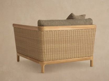 Close-up of Puglia Outdoor Teak Lounge Chair's corner. Natural teak arm, woven side, textured dark beige cushions and toss pillows.