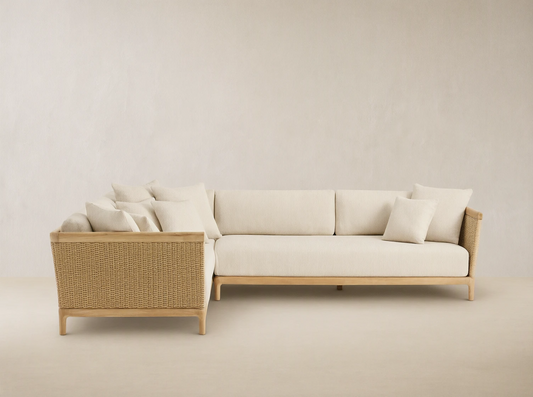 Puglia Outdoor Teak L-shaped Sectional with natural teak frame, light cream cushions, and woven wicker accents on an outdoor patio.